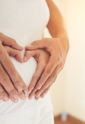 pregnant-woman-her-husband-hand-showing-heart-shape